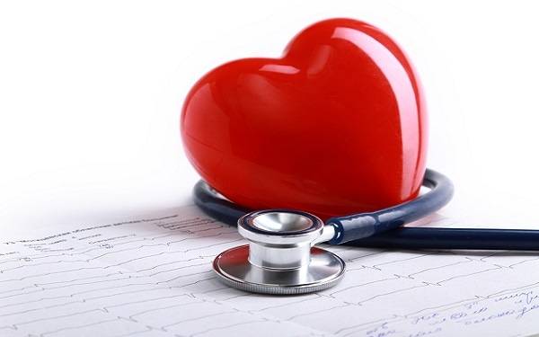 A stethoscope is wrapped around a red plastic heart on a heart scan printout.